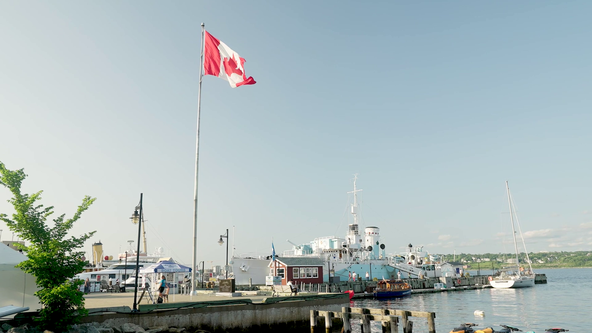 Canadian flag waving over the Halifax waterfront with docked boats and historic ships.